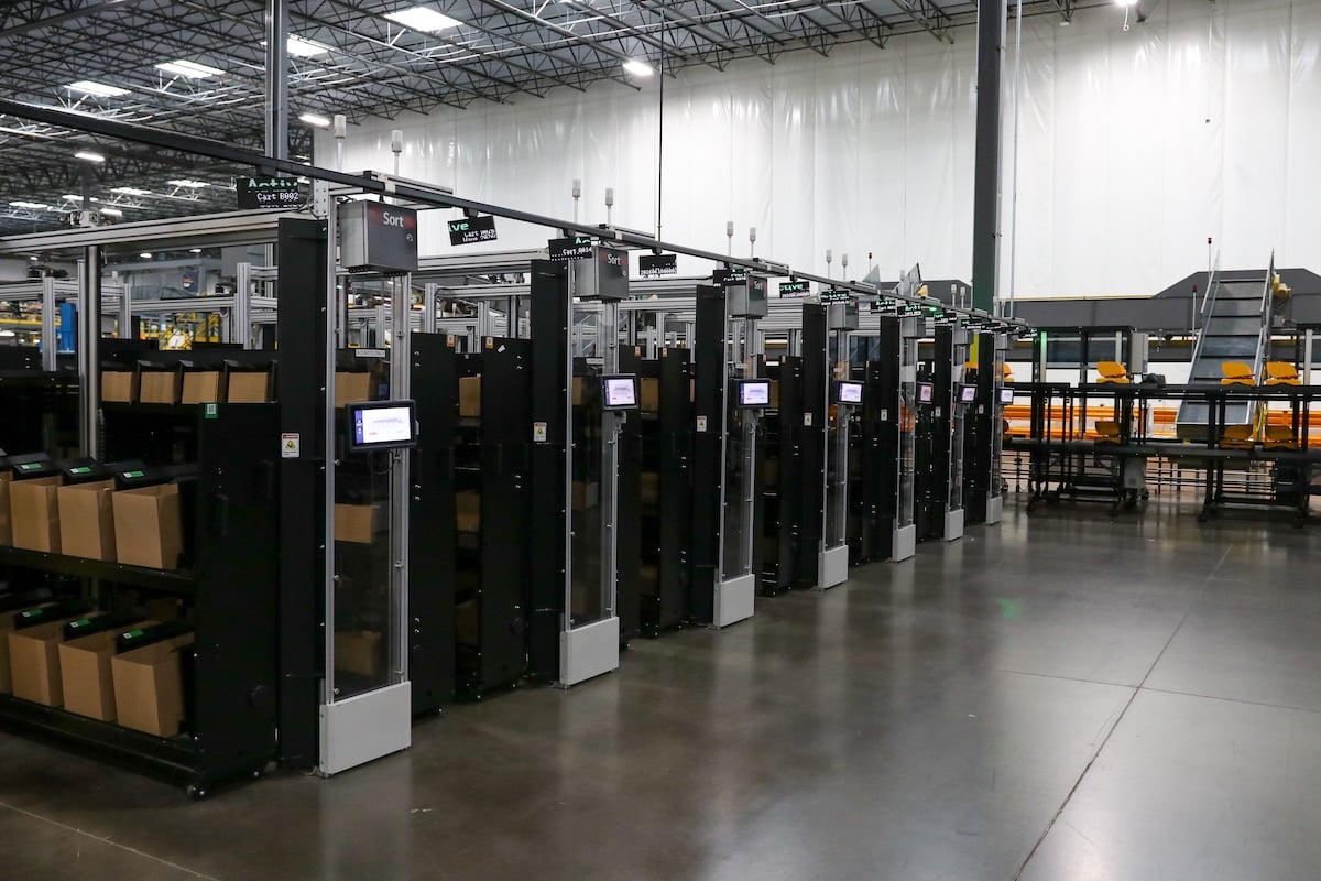 A row of tSort3D automated put wall modules in a distribution center, with carts of order cartons docked at each wall.
